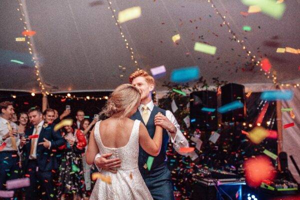 Bride and groom surrounded by confetti in front of an elegant sailcloth marquee.