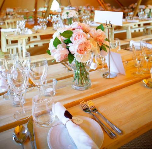 Beautiful table decorations and flowers on a rustic wooden table inside a Tipi Wedding.