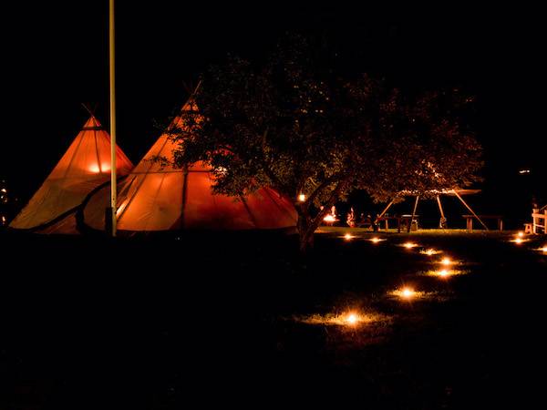 A whimsical fairy light path leads the way to a captivating tipi party at night, illuminating the surroundings with enchanting allure.