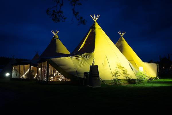 A striking yellow lit tipi tent stands ready for a festival, exuding a vibrant and captivating glow.