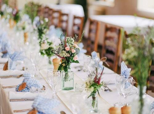 Beautiful flowers and decorations on a rectangular table with a white table cloth on a rustic wooden table inside a Tipi Wedding.