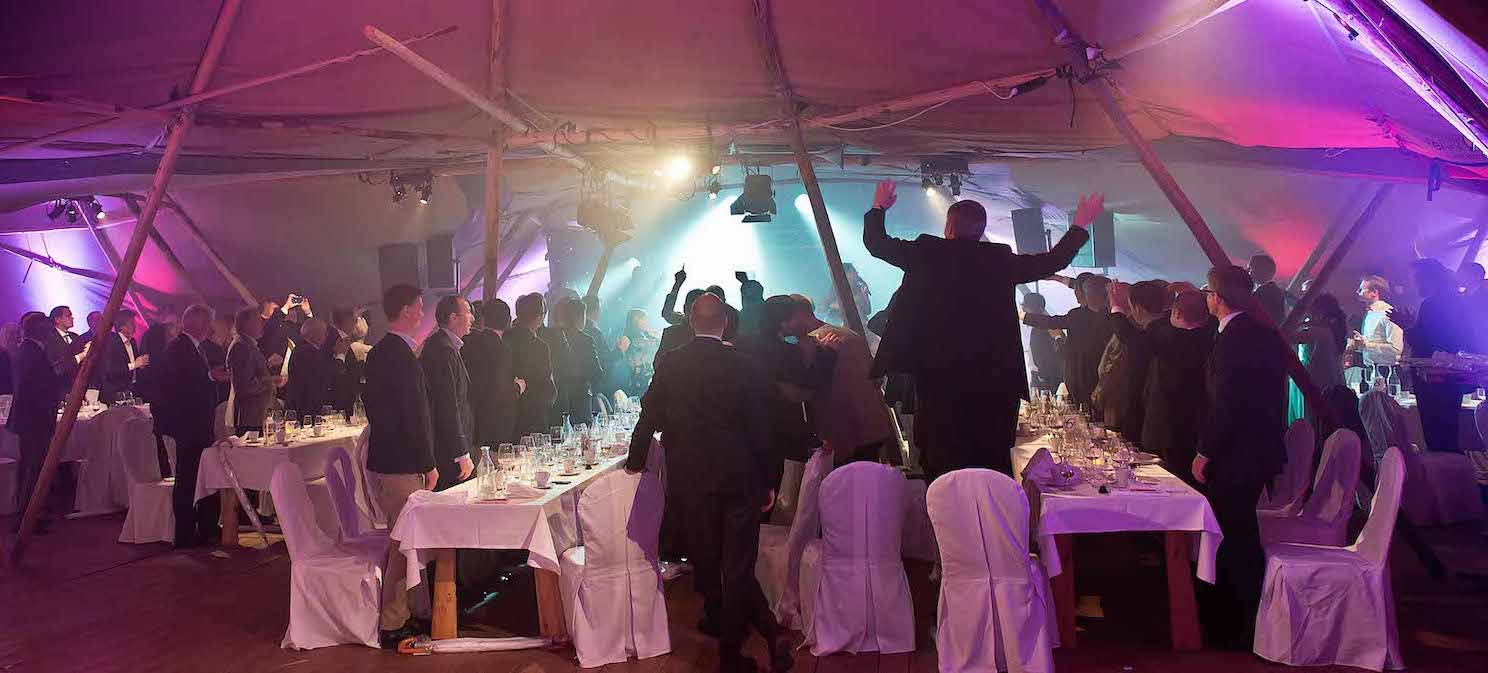 A black-tie Tipi party at Night with performers live on stage.