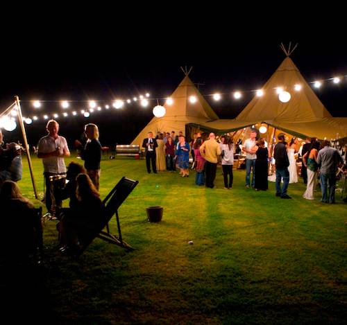 A captivating tipi party at night, surrounded by festoon lighting that emanates a warm and inviting glow.