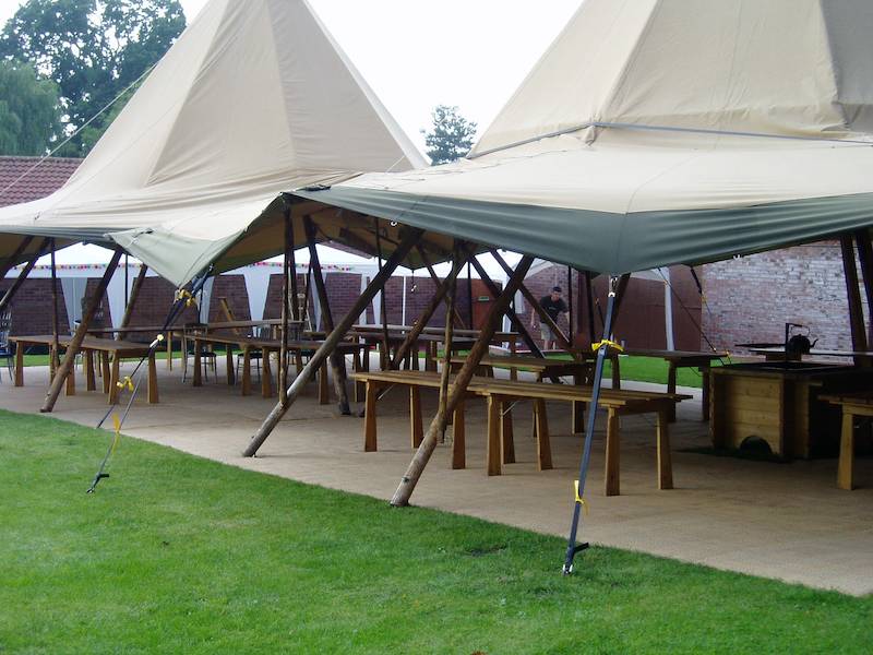 Two Tipis linked together with their sides up and an interior featuring rustic tables and benches ready for a corporate tipi event.
