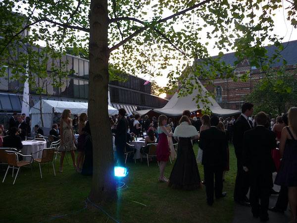 Smartly dressed students gather around a magnificent tipi at dusk during an Oxford University Ball.