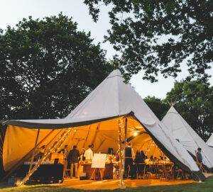 White Tipi hire for a wedding at dusk with orange glowing fairy lights wrapped around the wooden pillars.