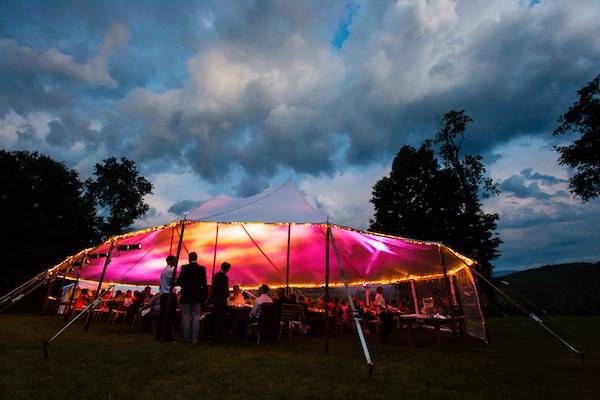 A large sailcloth tent with colourful lights and decorations, surrounded by a lively crowd at a festival at night.