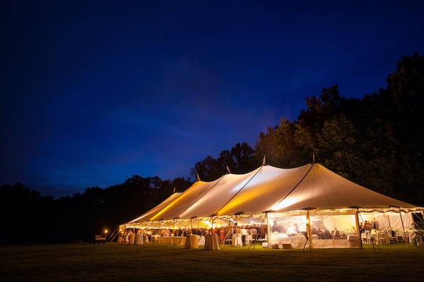A stylish Sperry Tent with draped fabric walls, glowing warmly in the dimly lit ambiance just after sunset, ready to host a fantastic party.