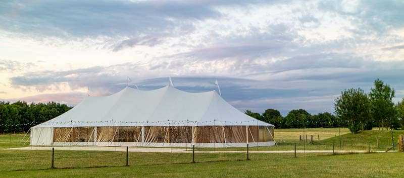 A Sperry Tent set up in a field in the evening for an event like a wedding or a party