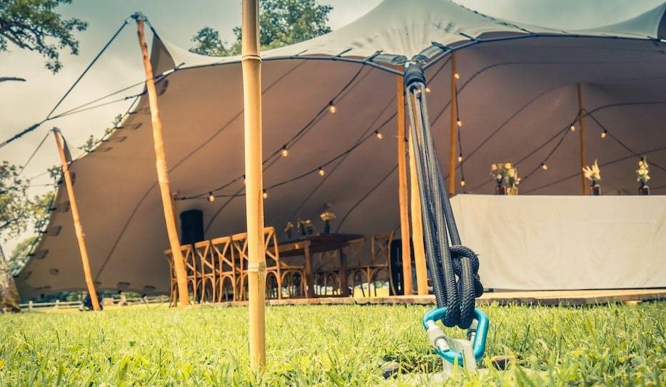 A stunning white stretch tent with wooden poles and decorative lighting for a magical atmosphere
