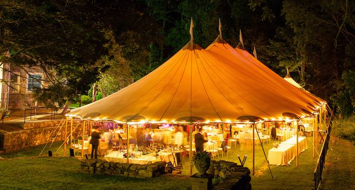 A magical scene unfolds as a wedding tent stands beneath the night sky, surrounded by trees. The soft glow of warm lights fills the air, creating an inviting atmosphere. Captured through a long exposure, part of the Birmingham Marquee Hire's enchanting wedding tent series.